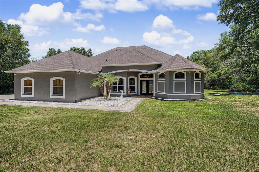 A single-story house with a gray stucco exterior, a brown shingled roof, and a paved walkway — 10933 PINTO DRIVE, HUDSON, FL