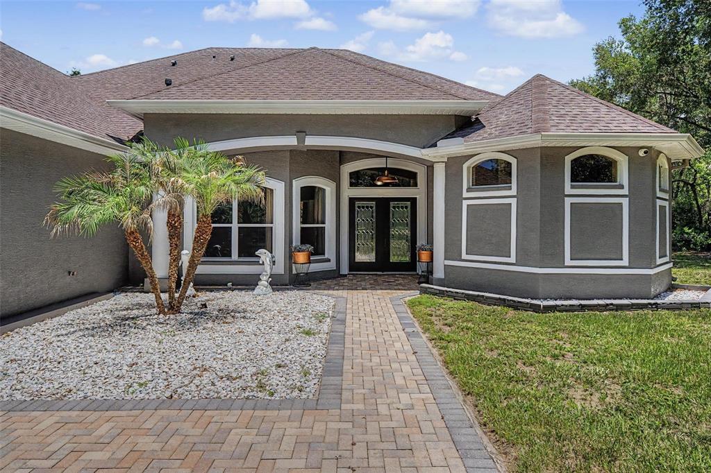 A gray stucco house features a brick paver walkway, a palm tree, and double front doors — 10933 PINTO DRIVE, HUDSON, FL
