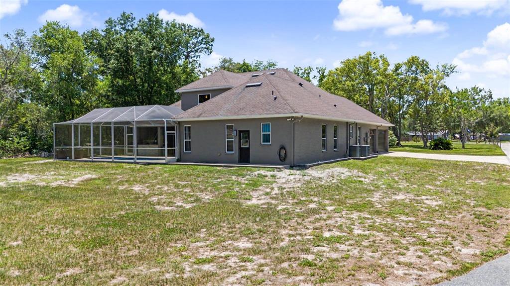 A tan house with a screened-in pool enclosure sits on a large, grassy lot — 10933 PINTO DRIVE, HUDSON, FL