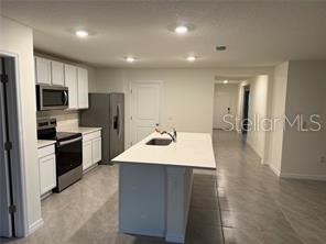 A kitchen features white cabinets, stainless steel appliances, a center island, and light tile flooring — 16953 NW 176TH WAY, ALACHUA, FL