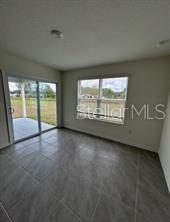 An empty room with gray tile flooring, a large window, and a sliding glass door — 16953 NW 176TH WAY, ALACHUA, FL