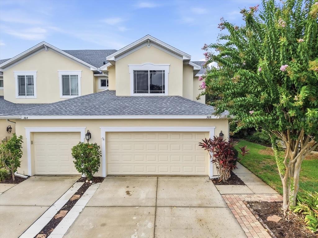 A two-story townhouse exterior features a beige facade, two garage doors, and a large tree — 368 HARBOR RIDGE DRIVE, PALM HARBOR, FL