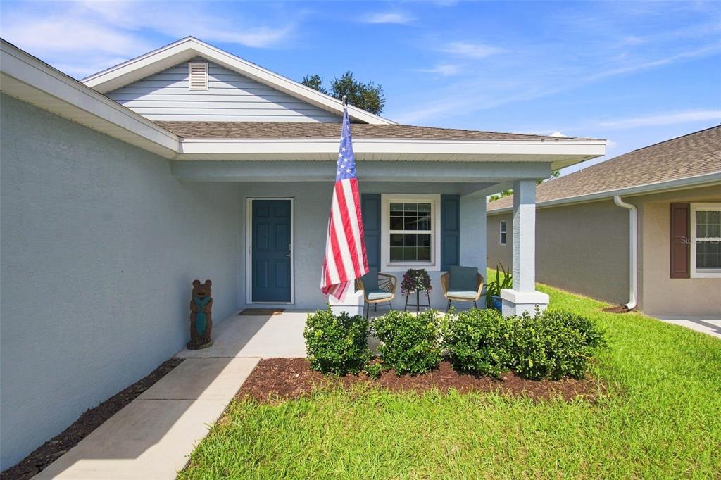A light blue house exterior features a covered front porch with an American flag — 10535 S DREW BRYANT CIRCLE, FLORAL CITY, FL