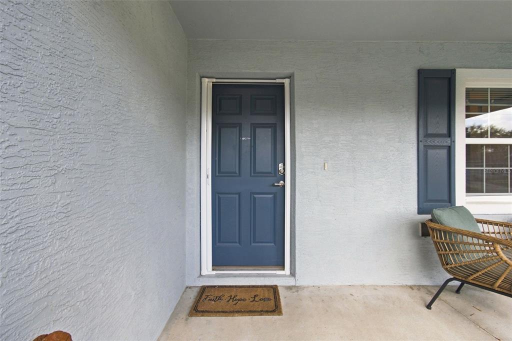 A blue front door with a welcome mat sits on a covered concrete porch — 10535 S DREW BRYANT CIRCLE, FLORAL CITY, FL
