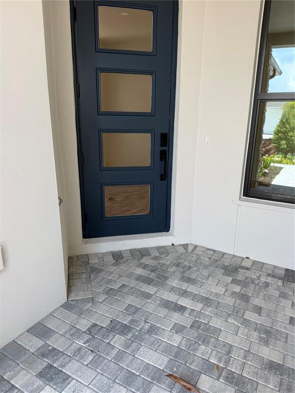 A dark blue front door with four glass panels sits beside a window on a paved porch — 5889 WINDBREAK COURT, APOLLO BEACH, FL