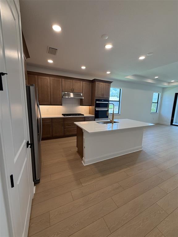 A kitchen features wood cabinets, a white island with a sink, and light wood flooring — 5889 WINDBREAK COURT, APOLLO BEACH, FL
