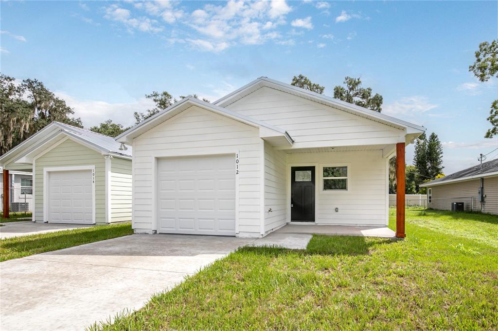 A white single-story house with a front-facing garage, a black door, and a concrete driveway — 1012 E HAZZARD, EUSTIS, FL