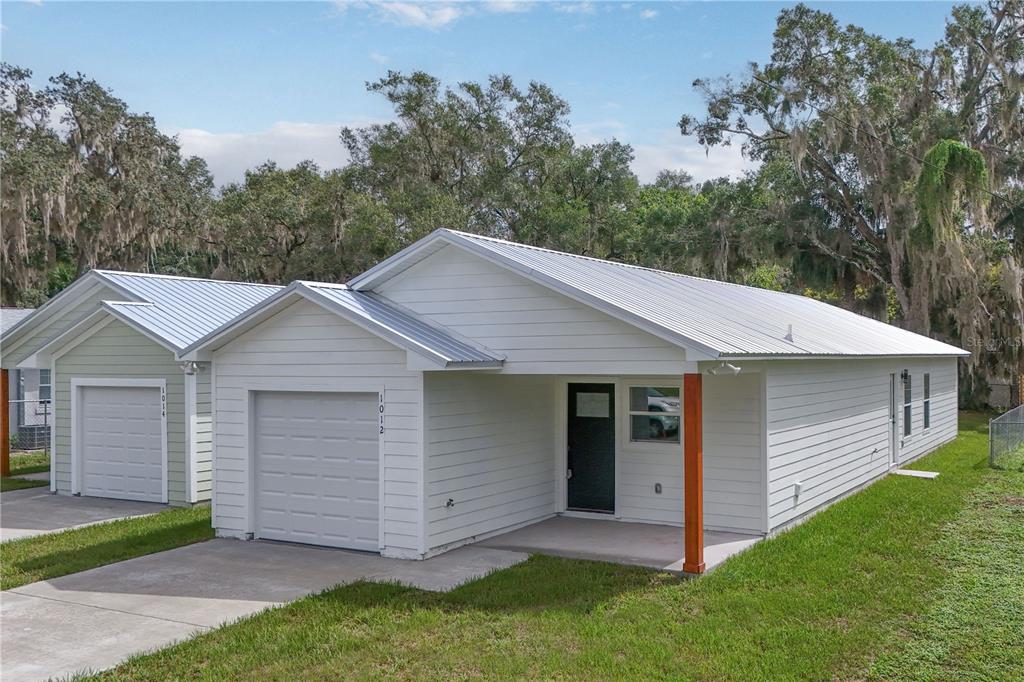 A white single-story house with a metal roof, a garage, and a covered front porch — 1012 E HAZZARD, EUSTIS, FL