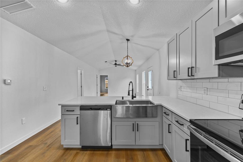A kitchen features gray cabinets, white countertops, a farmhouse sink, and stainless steel appliances — 1012 E HAZZARD, EUSTIS, FL