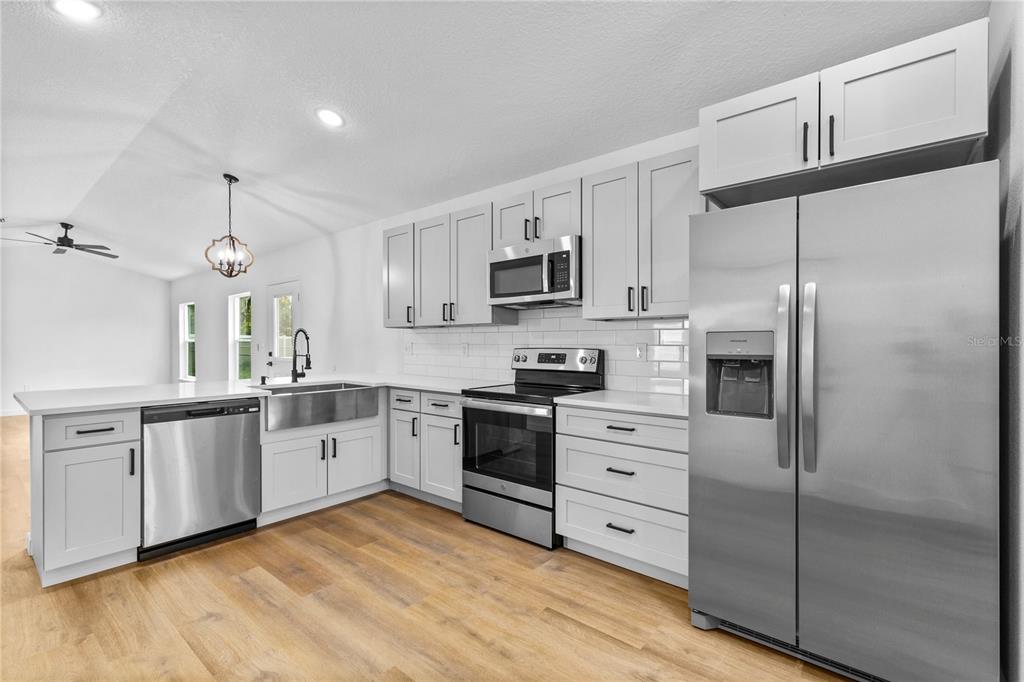 A modern kitchen features white cabinetry, stainless steel appliances, a farmhouse sink, and wood flooring — 1012 E HAZZARD, EUSTIS, FL