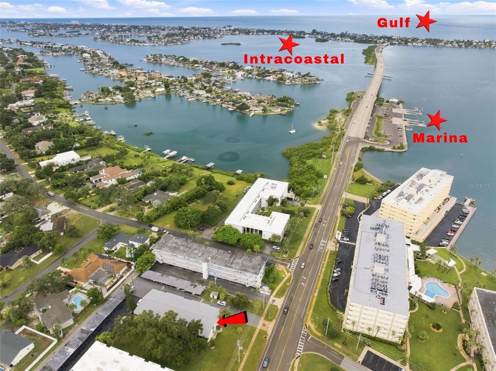 An aerial view shows a multi-story apartment complex near a bridge, marina, and coastal waterway — 2950 W BAY DRIVE UNIT B1, BELLEAIR BLUFFS, FL