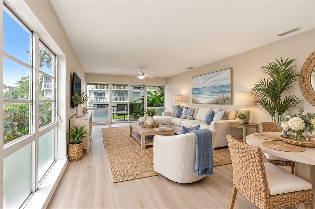 A bright, empty living room features light wood-look flooring, white walls, and large glass windows — 2950 W BAY DRIVE UNIT B1, BELLEAIR BLUFFS, FL