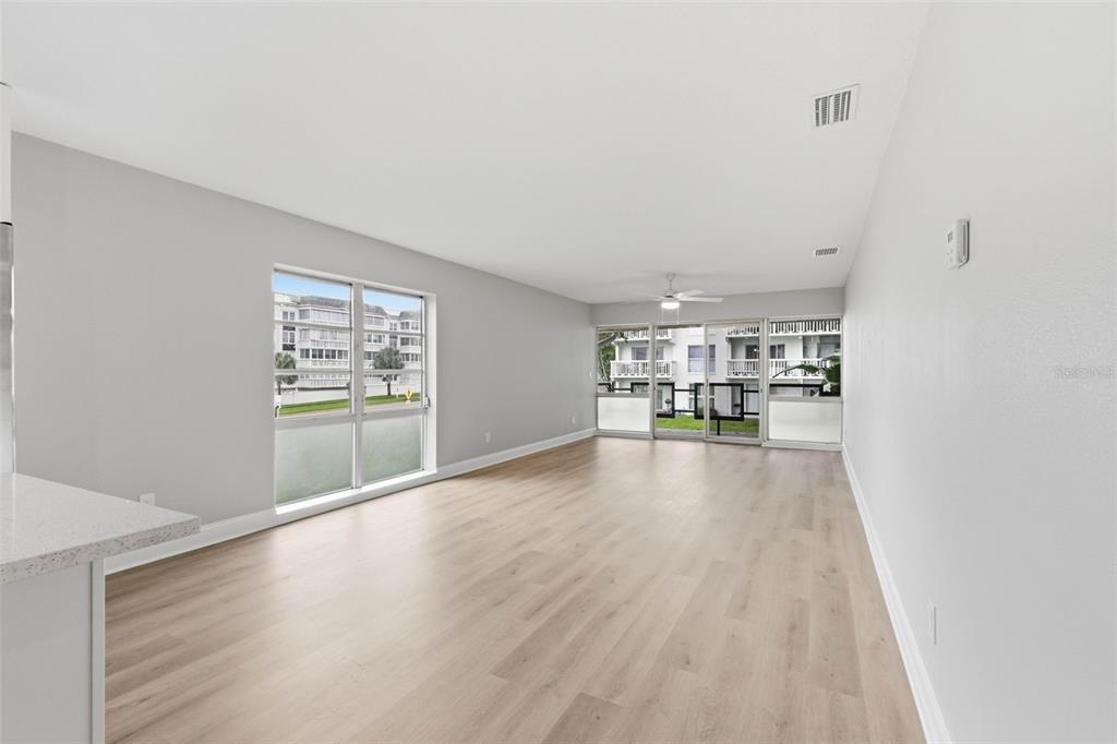 A bright, empty living room features light wood-look flooring, white walls, and large glass windows — 2950 W BAY DRIVE UNIT B1, BELLEAIR BLUFFS, FL