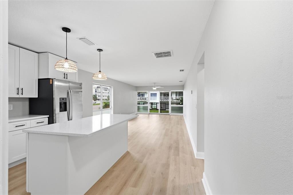 A bright, open-concept kitchen and living area features white cabinetry, a quartz island, and flooring — 2950 W BAY DRIVE UNIT B1, BELLEAIR BLUFFS, FL