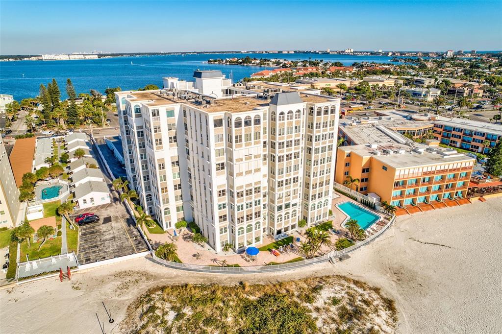 An aerial view shows a tall white apartment building situated on a sandy beach — 4950 GULF BOULEVARD UNIT 304, ST PETE BEACH, FL