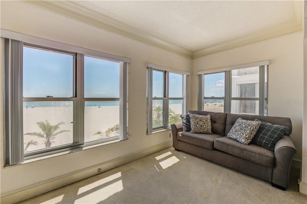 A sunroom with beige carpet and a gray sofa overlooks a sandy beach and ocean — 4950 GULF BOULEVARD UNIT 304, ST PETE BEACH, FL