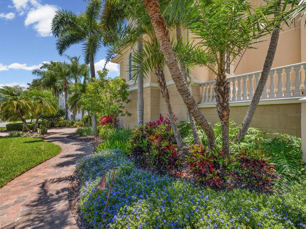 A brick walkway leads past a landscaped garden with palm trees toward a beige house — 6224 PASADENA POINT BOULEVARD, GULFPORT, FL