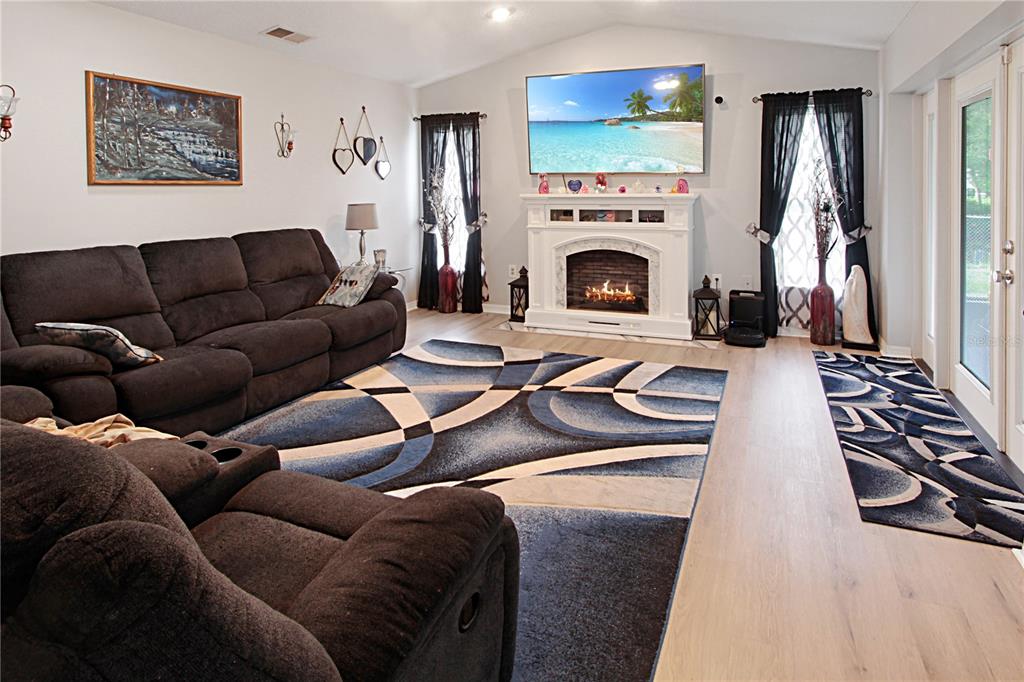 A living room features a fireplace, a large television, dark sofas, and patterned area rugs — 18 WESTON ROAD, LEESBURG, FL