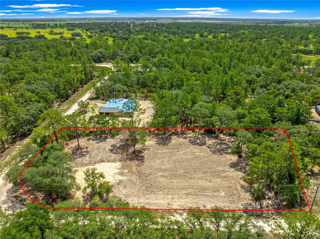 An aerial view shows a cleared rectangular lot surrounded by trees near a house — 8141 SW 122 AVENUE, DUNNELLON, FL