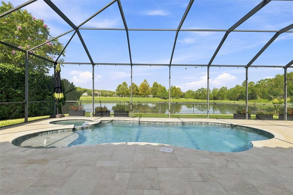 A screened-in swimming pool and spa overlook a lake with a metal fence — 2967 BARBOUR TRAIL, ODESSA, FL