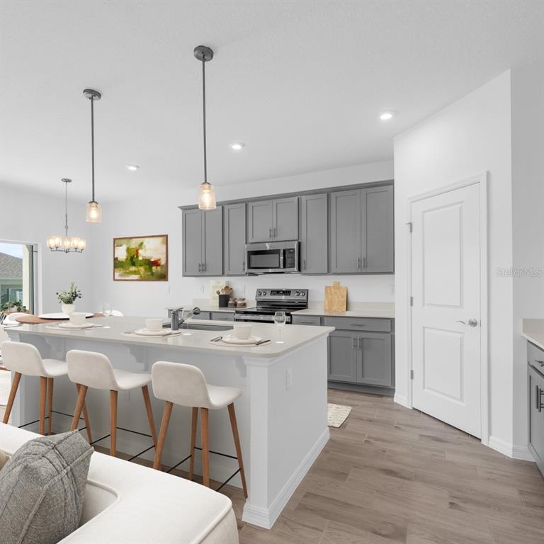 A modern kitchen features gray cabinets, a white island with bar stools, and wood-look flooring — 1090 CLAY BOULEVARD, TAVARES, FL