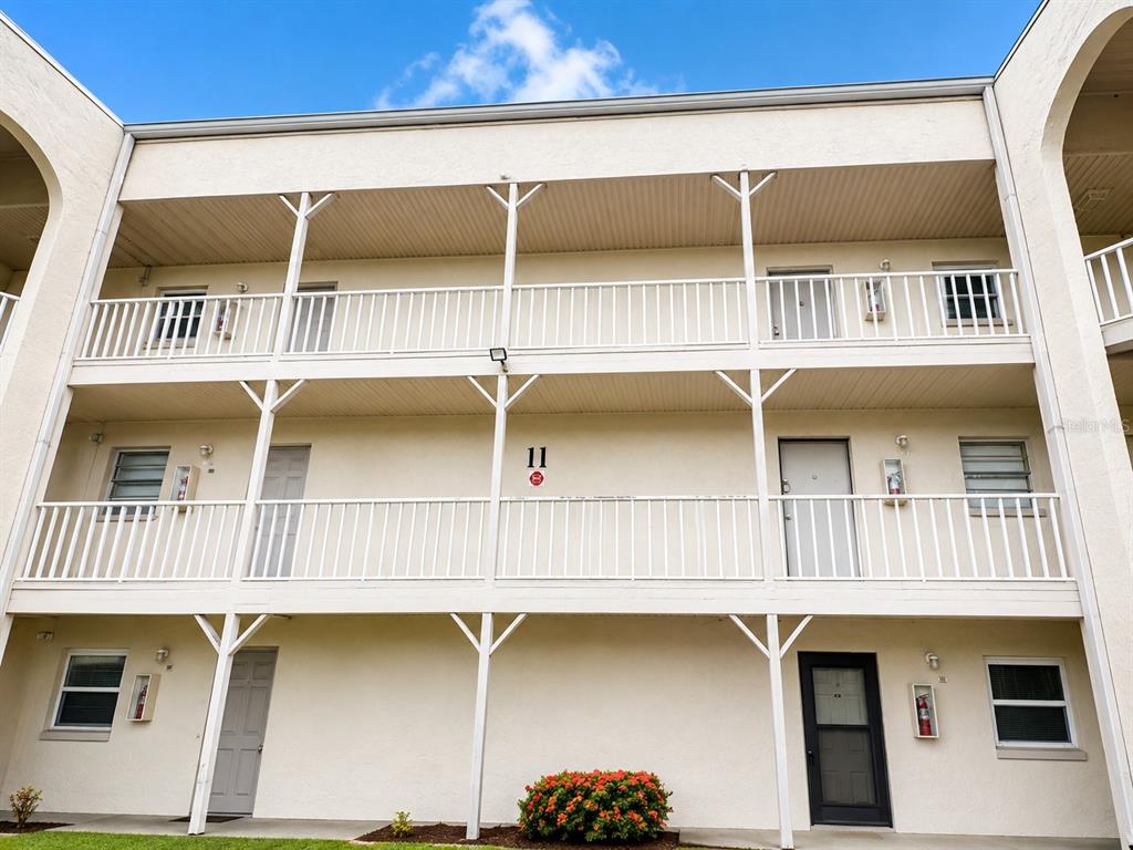 A three-story apartment building exterior features white balconies, support pillars, and multiple entry doors — 2625 STATE ROAD 590 UNIT 1123, CLEARWATER, FL