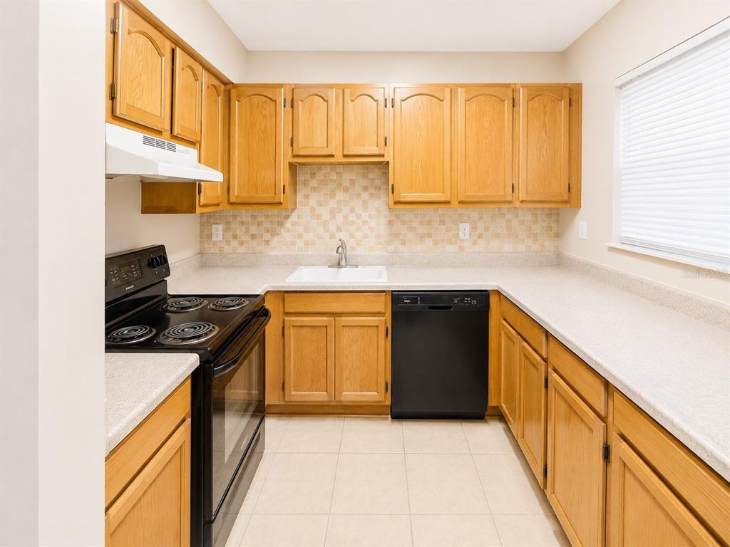 A kitchen features oak cabinets, black appliances, a tiled backsplash, and light-colored countertops — 2625 STATE ROAD 590 UNIT 1123, CLEARWATER, FL