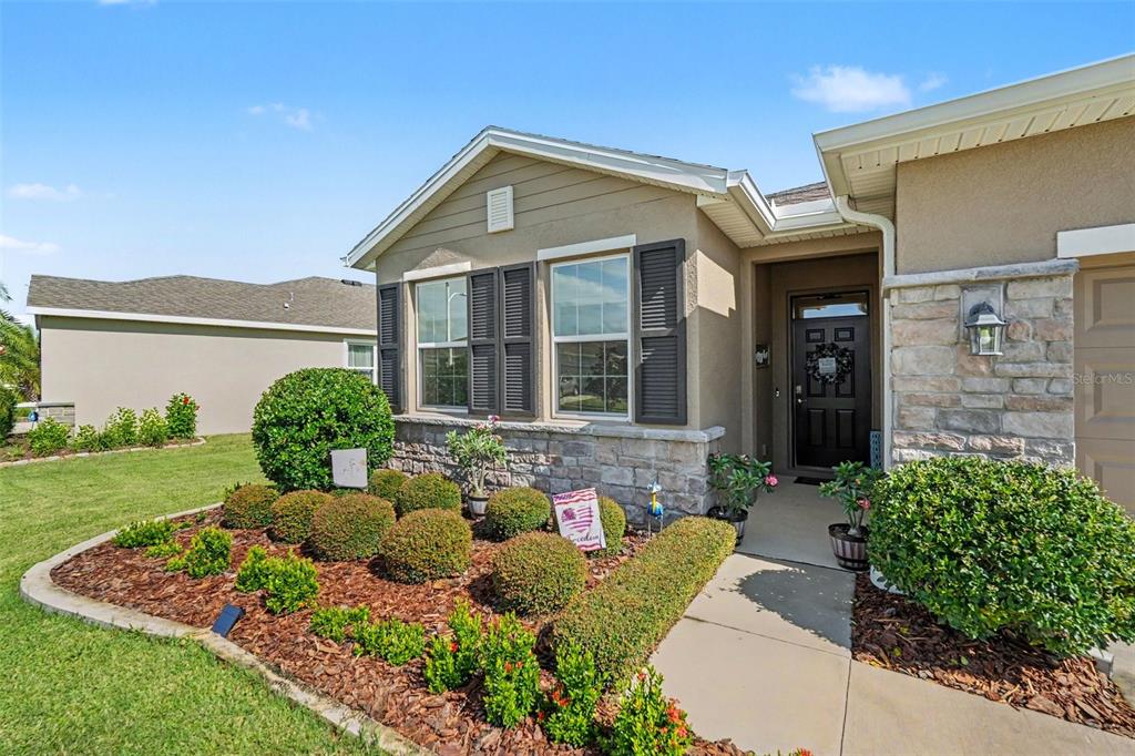 A tan house exterior features stone accents, dark shutters, and a landscaped front yard — 38387 SPRINGHEAD LN, ZEPHYRHILLS, FL