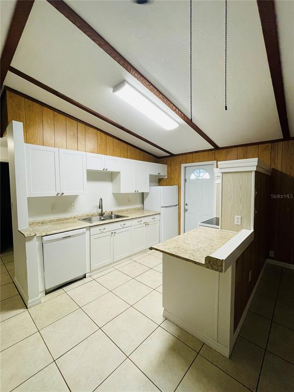 A kitchen with white cabinets, light countertops, tile flooring, and wood-paneled walls under a vaulted ceiling — 1335 S MARTIN LUTHER KING JR AVENUE, CLEARWATER, FL