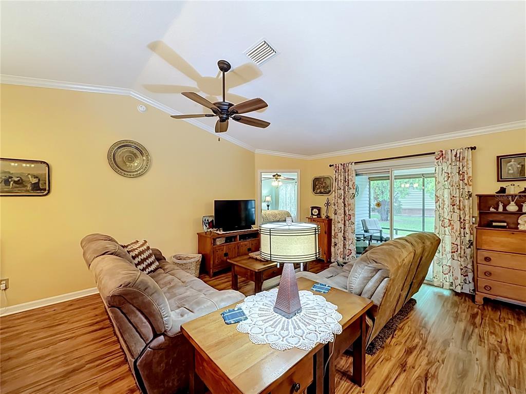 A living room features light yellow walls, wood-look flooring, two brown sofas, and a ceiling fan — 1016 MATTHEW AVENUE, LADY LAKE, FL
