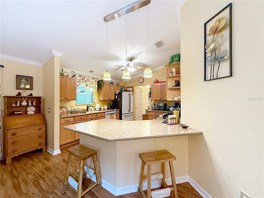 A kitchen features light wood cabinets, a granite-topped island with two stools, and wood flooring — 1016 MATTHEW AVENUE, LADY LAKE, FL