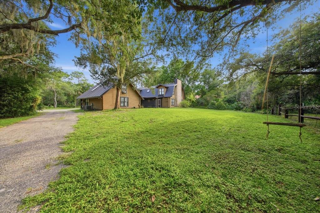 A two-story log cabin sits on a large grassy lot with a gravel driveway — 1630 STILLMEADOW ROAD, DELTONA, FL