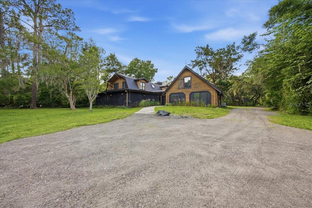A two-story log cabin home with a gravel driveway and a large screened-in porch — 1630 STILLMEADOW ROAD, DELTONA, FL