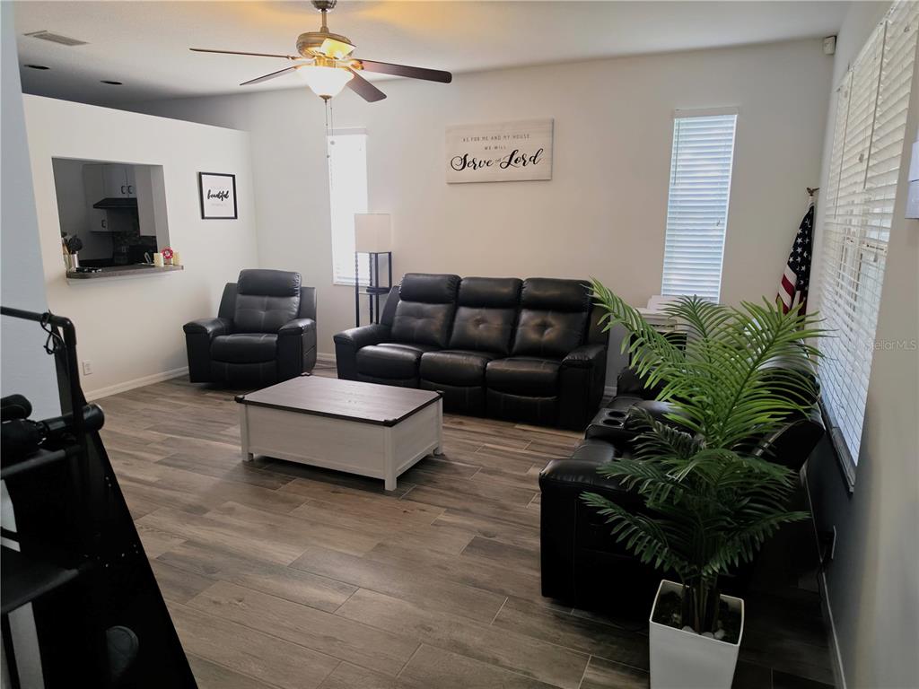 A living room features dark leather furniture, a white coffee table, and wood-look tile flooring — 3328 70TH COURT E, PALMETTO, FL