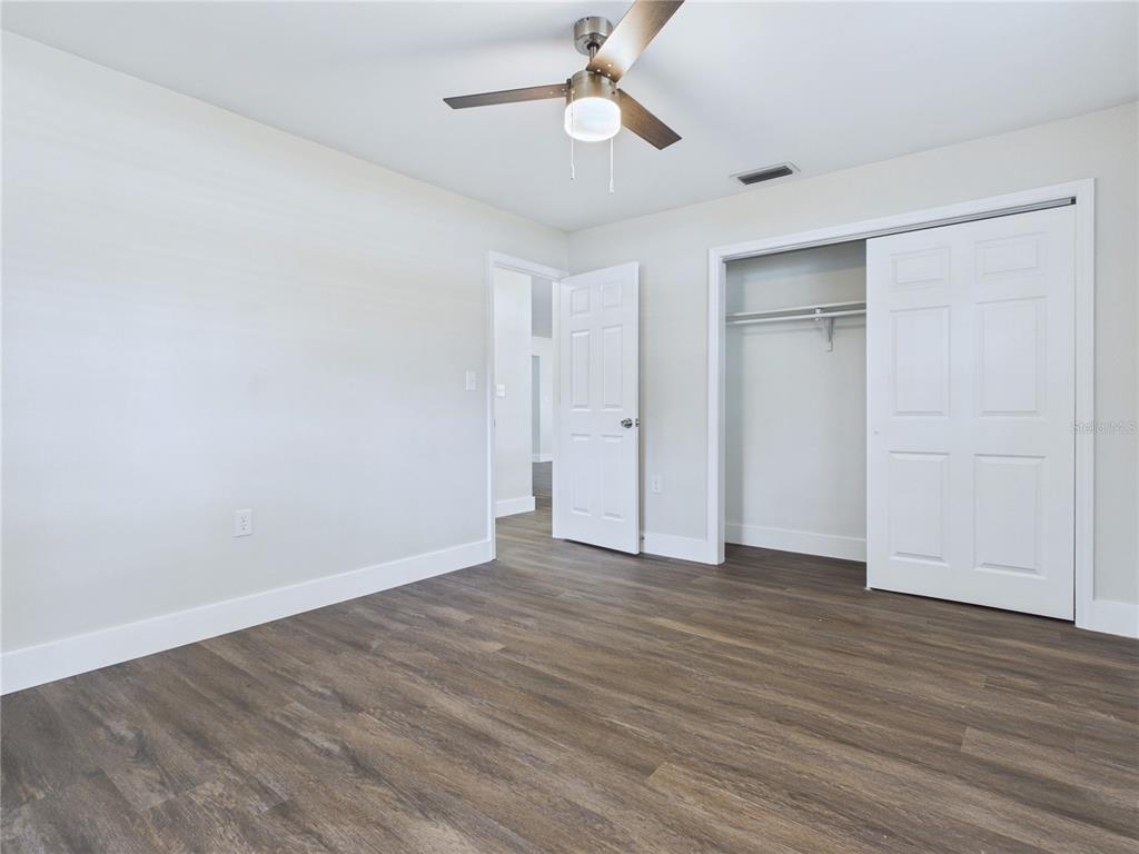 A bedroom features wood-look flooring, a ceiling fan, a white door, and a sliding closet — 457 WATER ROAD, OCALA, FL
