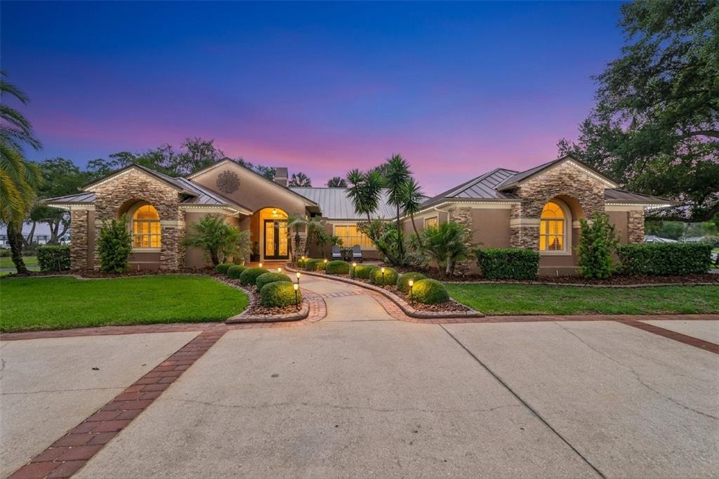 A single-story house with a stone facade, metal roof, and a curved walkway at dusk — 29650 SQUIRREL POINT ROAD, TAVARES, FL