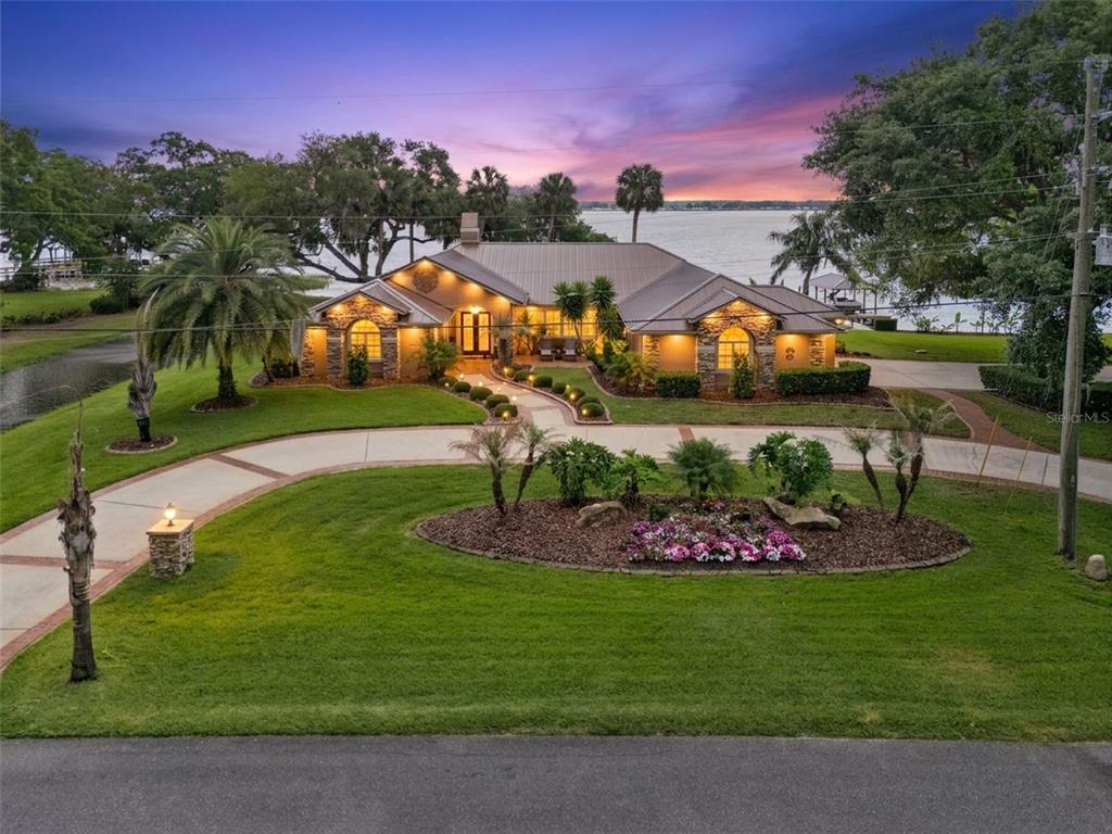 A single-story house with a metal roof and stone facade sits on a waterfront lot — 29650 SQUIRREL POINT ROAD, TAVARES, FL