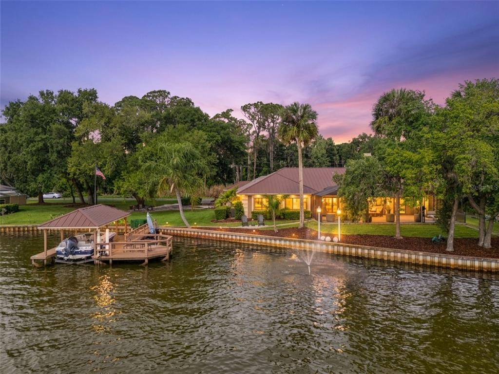 A waterfront house with a boat dock, a fountain, and a lawn at sunset — 29650 SQUIRREL POINT ROAD, TAVARES, FL