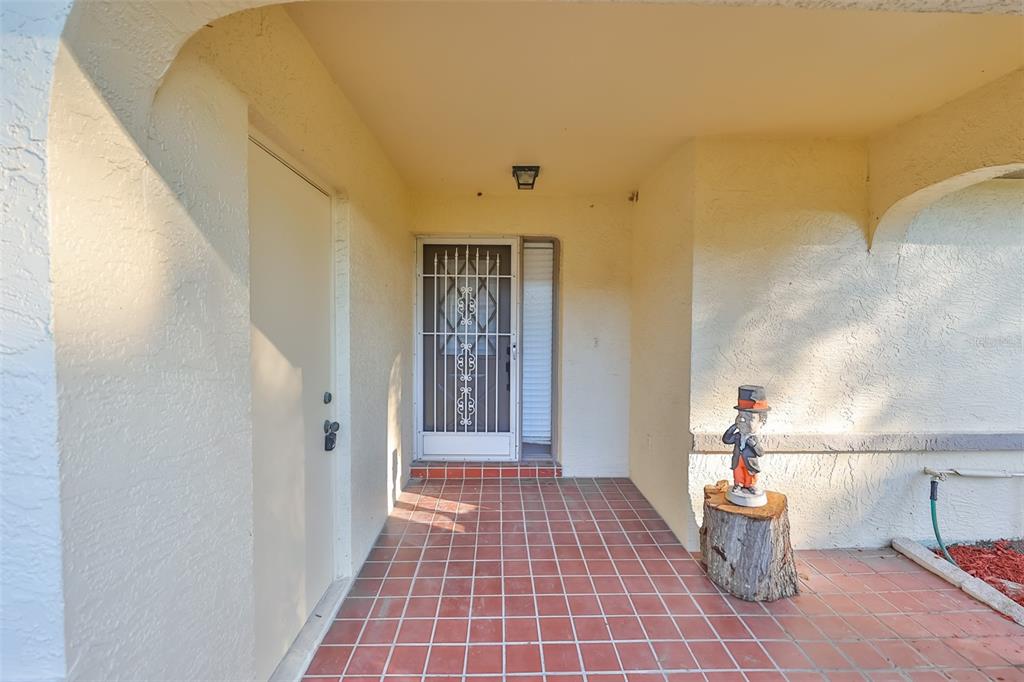 A covered entryway features a tiled floor, a security screen door, and a decorative gnome statue — 2321 LANCASTER DRIVE, SUN CITY CENTER, FL