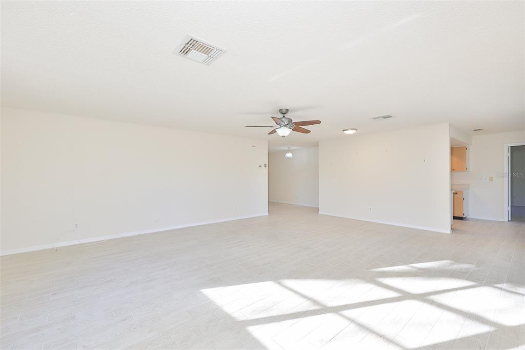 A spacious, empty living room features light-colored tile flooring, a ceiling fan, and neutral walls — 2321 LANCASTER DRIVE, SUN CITY CENTER, FL