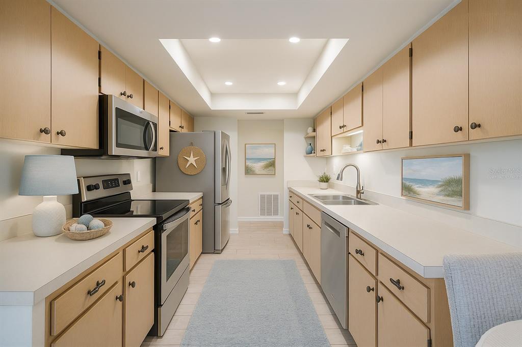 A galley-style kitchen features light wood cabinets, stainless steel appliances, and white countertops — 2321 LANCASTER DRIVE, SUN CITY CENTER, FL
