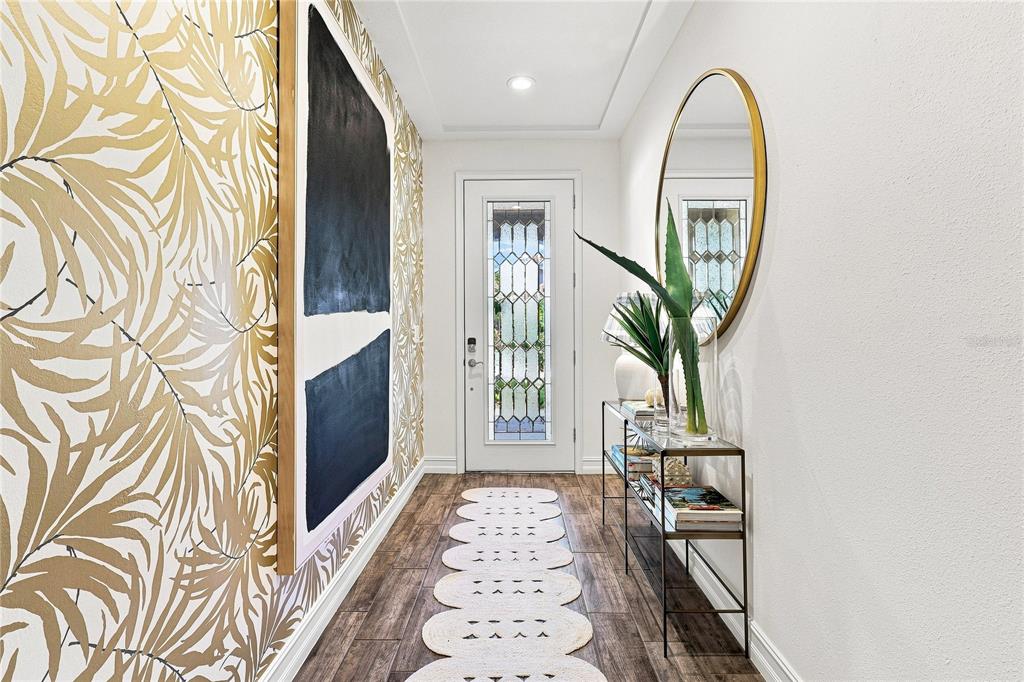 A bright entryway features gold palm-leaf wallpaper, a console table, a round mirror, and flooring — 12320 TERRACOTTA DRIVE, BRADENTON, FL