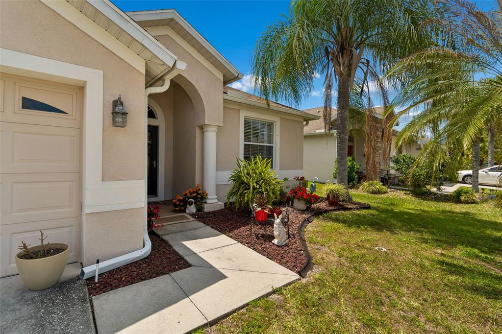 The exterior of a beige single-story house features a front walkway, landscaping, and a palm tree — 4027 LANGDRUM DRIVE, WESLEY CHAPEL, FL