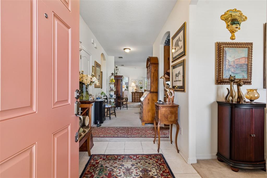 A view through an open pink door into a tiled entryway leading to a carpeted hallway — 4027 LANGDRUM DRIVE, WESLEY CHAPEL, FL