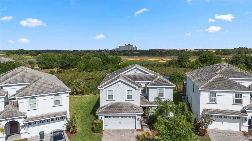 An aerial view shows three two-story houses with tiled roofs and driveways near a golf course — 1571 PALMERO WAY, CHAMPIONS GATE, FL