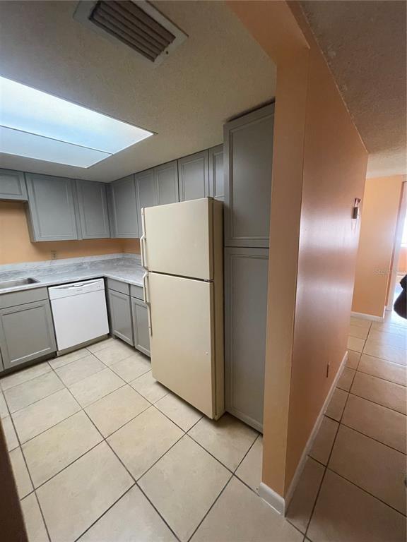 A kitchen features gray cabinets, a white refrigerator, a dishwasher, and light-colored tile flooring — 549 FAIRWAYS DRIVE UNIT A, OCALA, FL