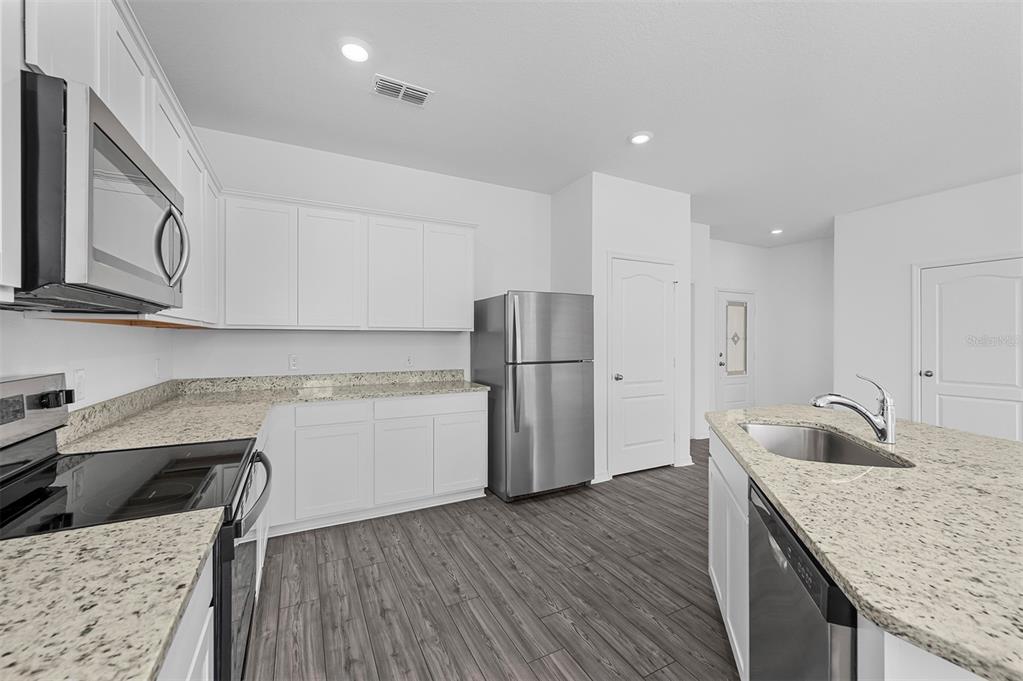 A kitchen features white cabinets, granite countertops, stainless steel appliances, and wood-look flooring — 556 BAY LEAF DRIVE, POINCIANA, FL
