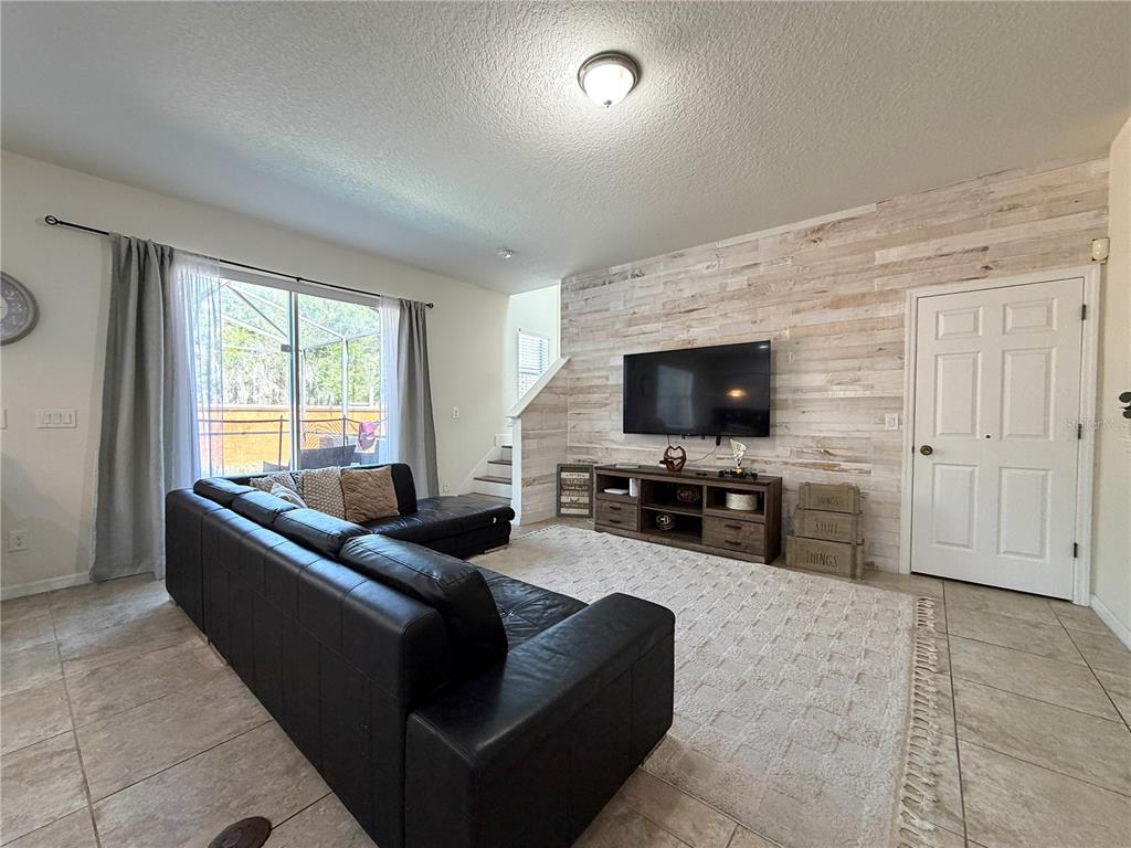 A living room features a black sectional sofa, a wood-paneled accent wall, and a television — 720 LAS FUENTES DRIVE, KISSIMMEE, FL