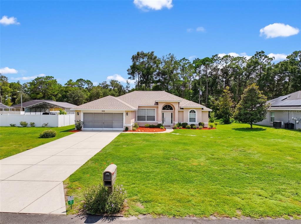 A single-story house with a beige exterior, a two-car garage, and a large front lawn — 9700 N KENDALL WAY, CITRUS SPRINGS, FL
