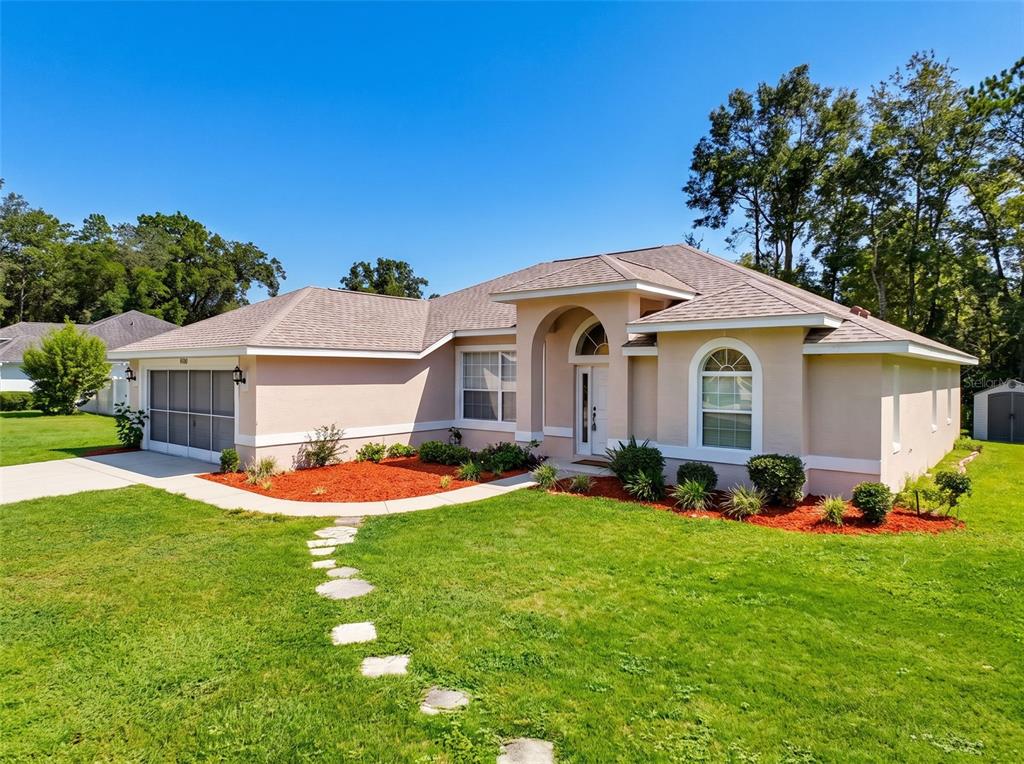 A single-story tan house with a two-car garage, arched entryway, and a stone walkway — 9700 N KENDALL WAY, CITRUS SPRINGS, FL